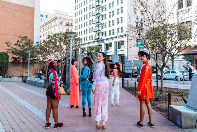 A group of friends wearing colorful outfits looks back at the camera while walking down the street. 
