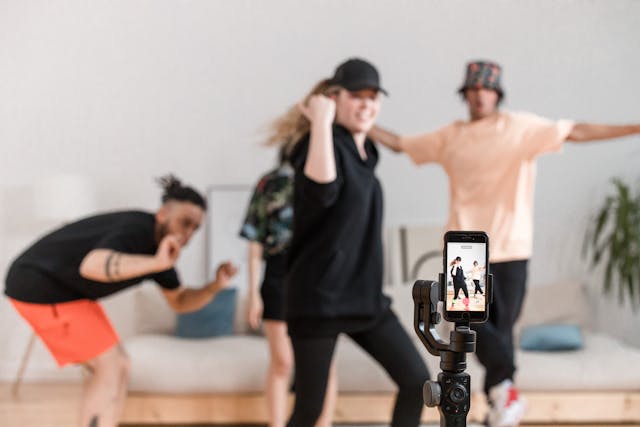 Three people dancing in front of a phone recording a video.
