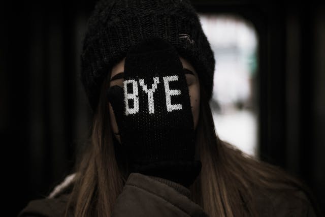 A woman covers her face with a hand in a black glove printed with the word “Bye.”