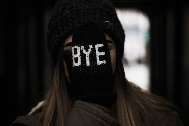 A woman covers her face with a hand in a black glove printed with the word “Bye.”
