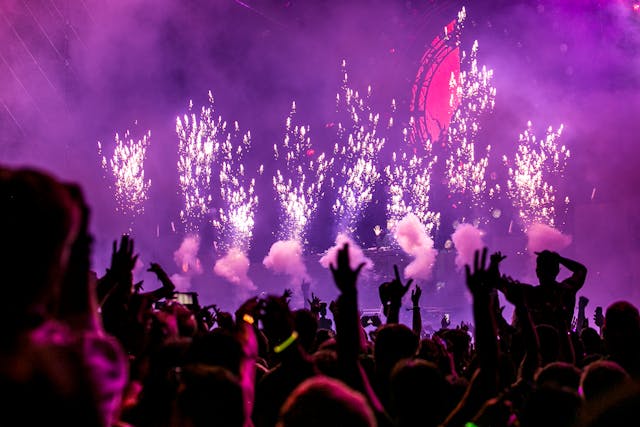 A big audience cheers as fireworks go off onstage at a concert. 
