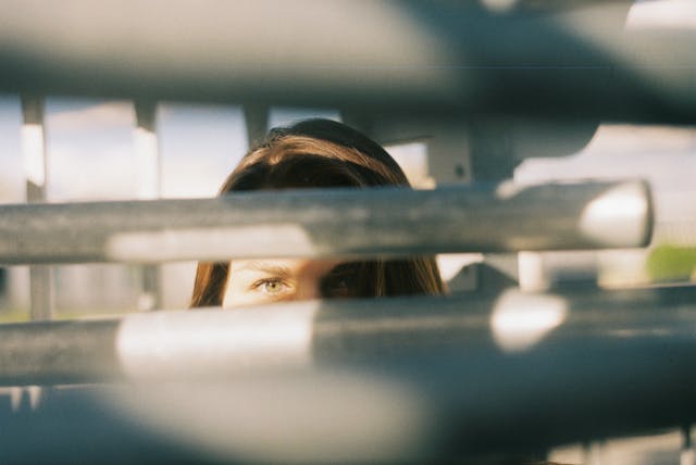 Een vrouw kijkt naar de camera terwijl ze achter metalen relingen staat. 