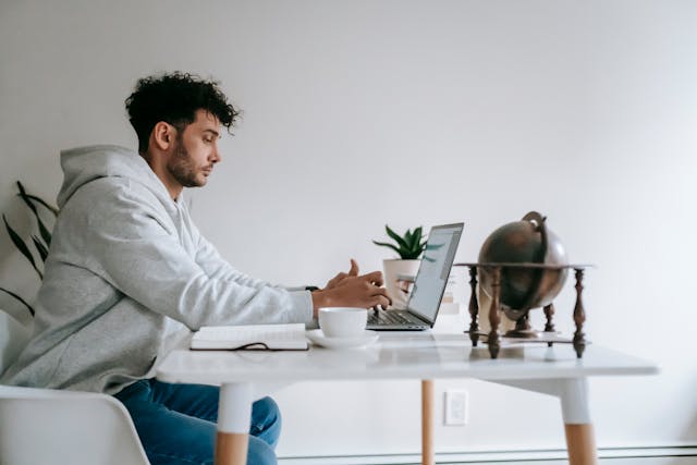 A man sits on a desk and browses TikTok videos on his laptop. 

