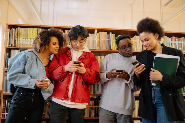 Estudantes dentro de uma biblioteca percorrem vídeos de tendências em seus telefones.