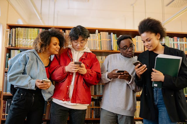 Elevii din interiorul unei biblioteci răsfoiesc videoclipuri la modă pe telefoanele lor. 