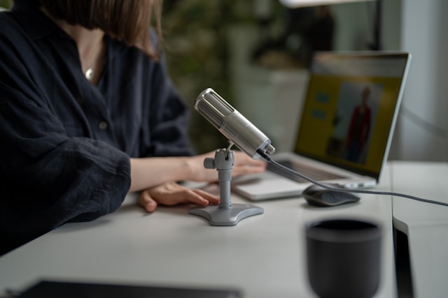 Uma pessoa sentada em frente a um laptop e um microfone.