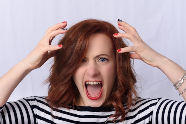 A woman screams and has her hands hovering over her head. 
