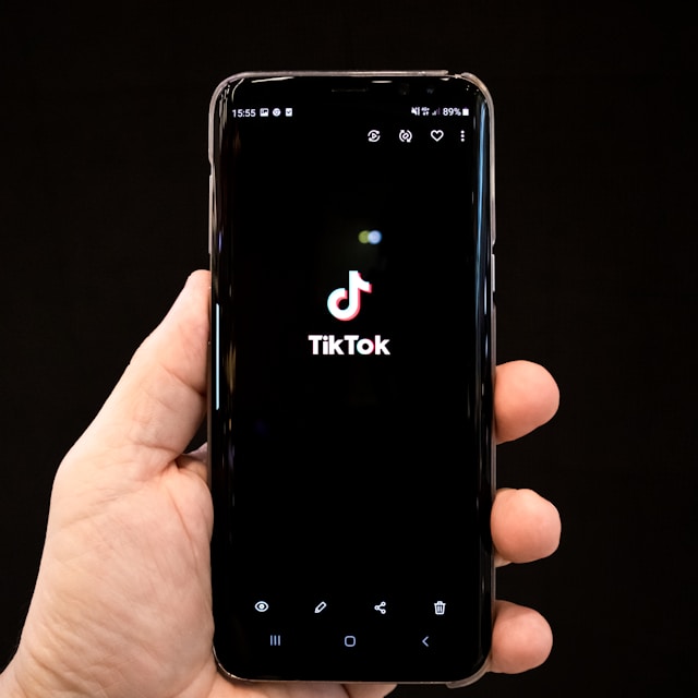 TikTokのロゴが表示された携帯電話を持つ人物。