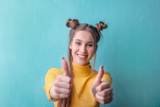 Uma jovem com um suéter amarelo dá dois polegares para cima. 