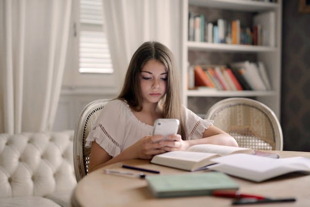 A girl scrolls her phone while she sits at a table.