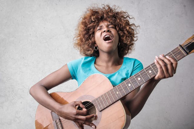 A woman sings as she plays the guitar. 
