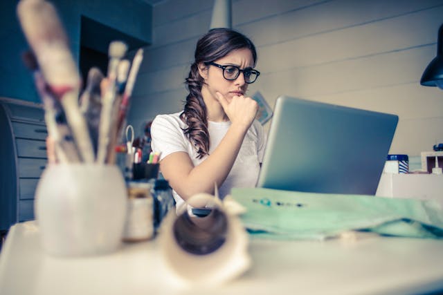 A woman frowns as she stares at her laptop screen.