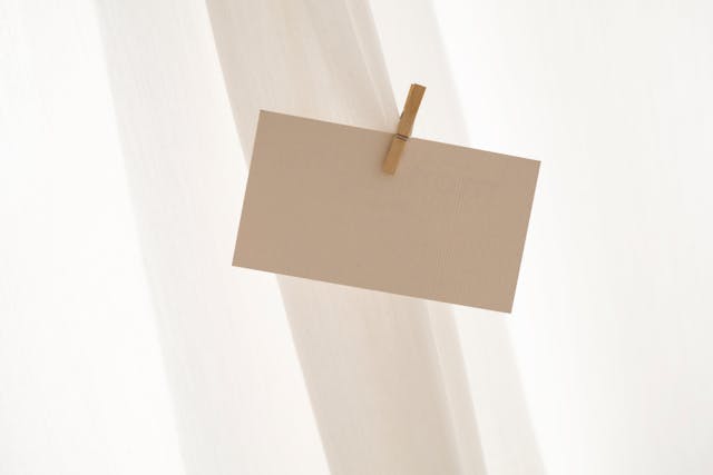 Um pequeno pedaço de papelão em branco é preso a uma cortina com um alfinete de roupa.