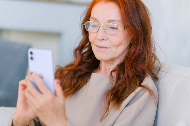 Uma mulher idosa de óculos navega no TikTok em seu celular.