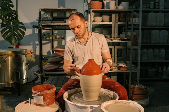 A man paints a clay vase as it turns on a pottery wheel.
