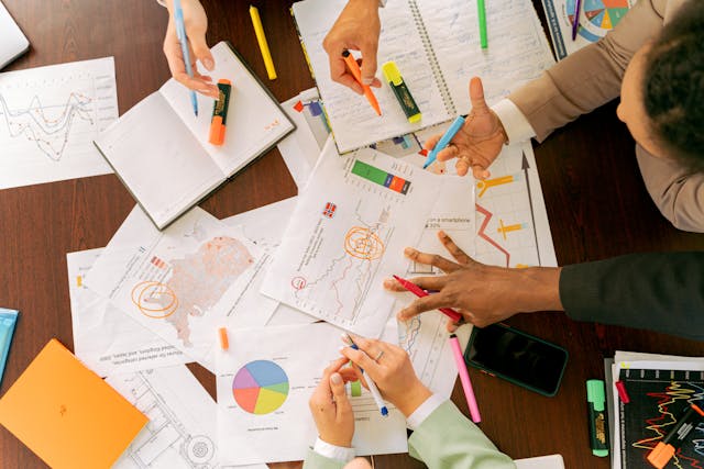 A group of people analyze data printed on pieces of paper scattered on a table. 
