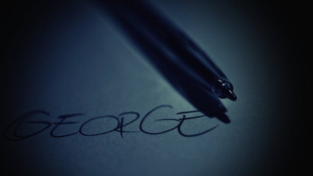 A pen rests on a piece of paper with the name “George” written on it.