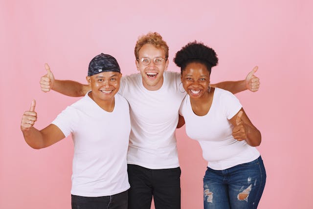 Three people in white shirts smile for the camera and give thumb-up signs.