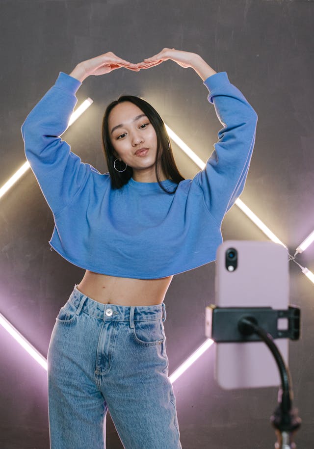 A woman in a cropped sweater poses in front of her phone.