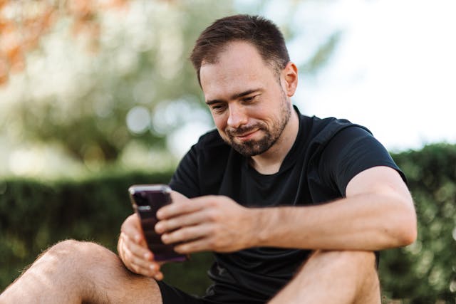 Een man lacht terwijl hij naar zijn telefoonscherm kijkt.
