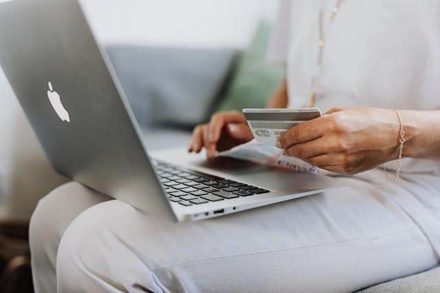 O persoană introduce informațiile cardului său de credit în laptop pentru a finaliza o achiziție online.