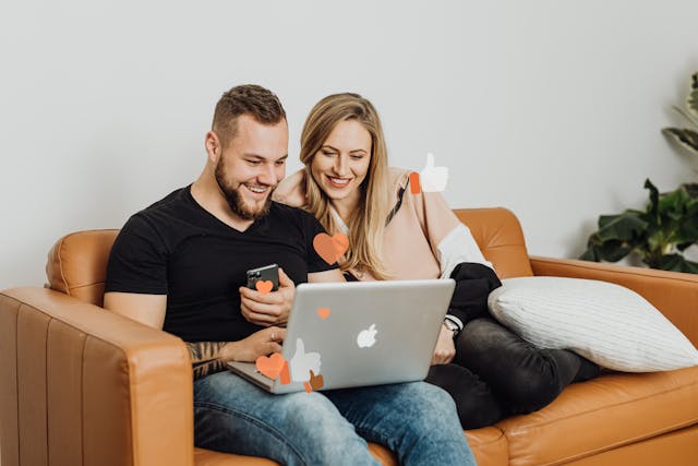 Um casal em um sofá sorri enquanto verifica seu laptop. 