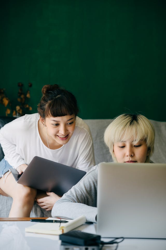 Two women talk while typing on their computers.