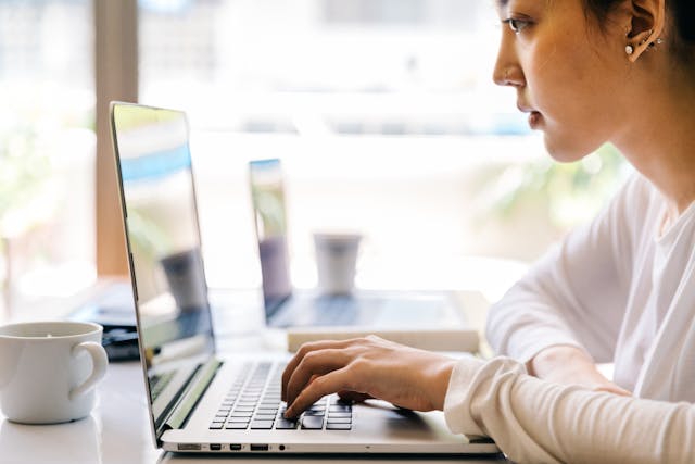 A woman sits in a cafe and types on her laptop. 
