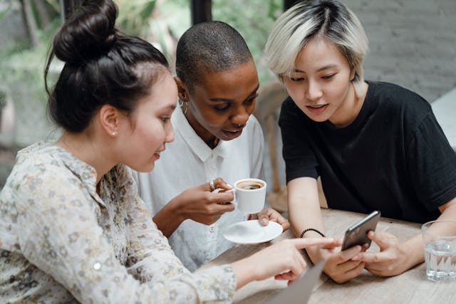 Trois amies sont assises dans un café en plein air et utilisent un téléphone pour consulter les mises à jour des médias sociaux. 