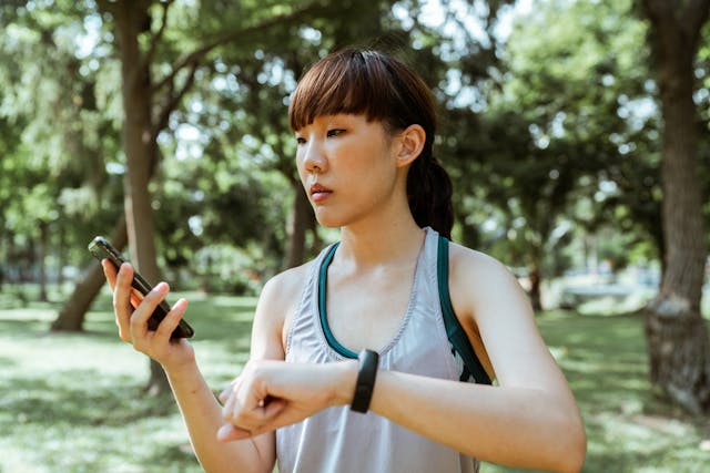 A woman pauses her run through the park to check her phone. 

