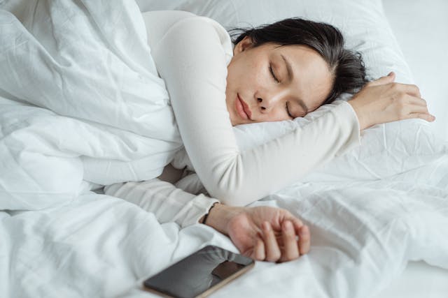 A woman sleeps in bed with her phone beside her. 

