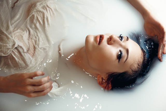Uma mulher posa para a câmera enquanto flutua em um líquido branco. 