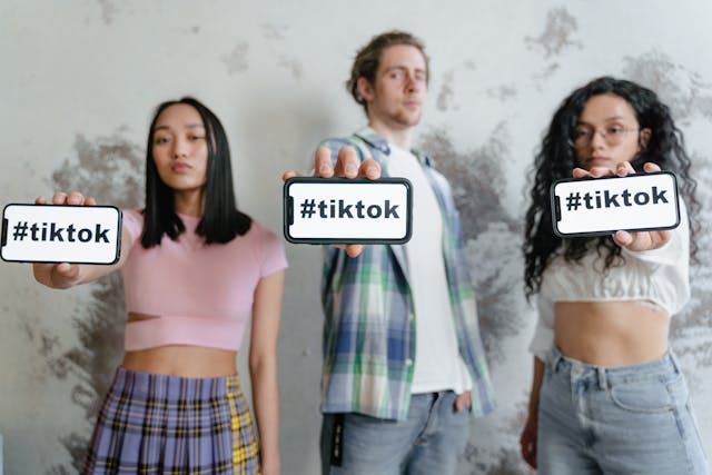 三个年轻人手持智能手机，屏幕上显示着 "#tiktok"。 