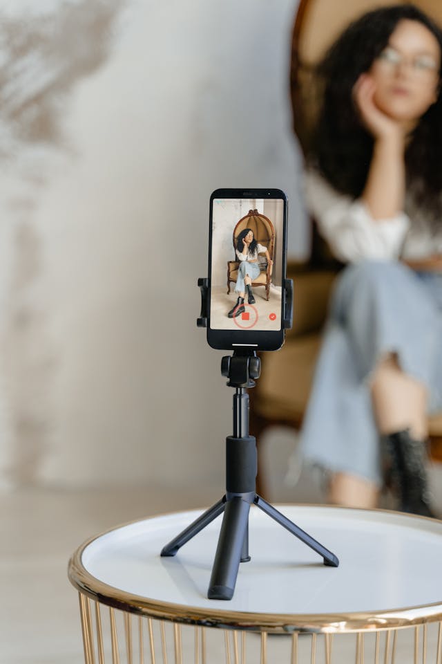 A woman sits in a chair in front of her cell phone.
