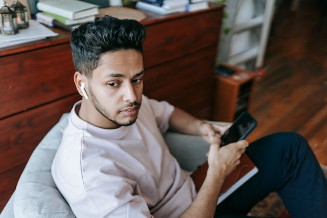 Een man zit in een stoel met zijn telefoon in zijn hand en een Airpod in zijn oor.