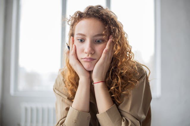 Een vrouw kijkt verbijsterd en legt haar gezicht tussen haar handen. 