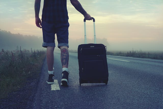 A man pulls his luggage as he walks on a deserted road. 