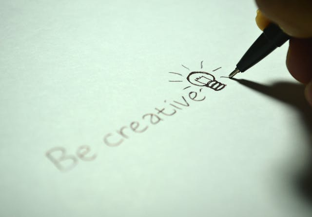 A person writes the words “Be creative” on white paper.