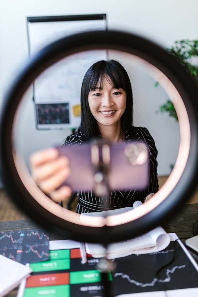 A woman with a ring light records herself on her cell phone.