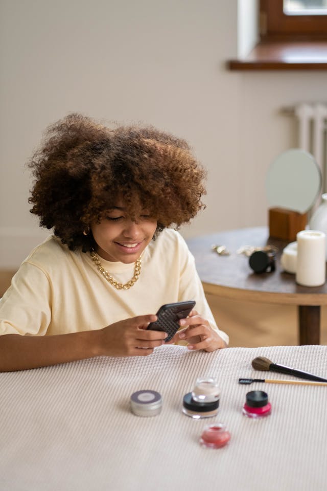 A smiling woman takes a photo of makeup items lain out on a table to post to her TikTok.