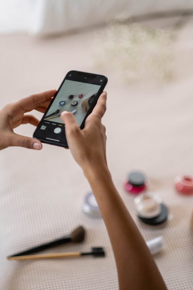 A person takes photos of makeup products on a table.