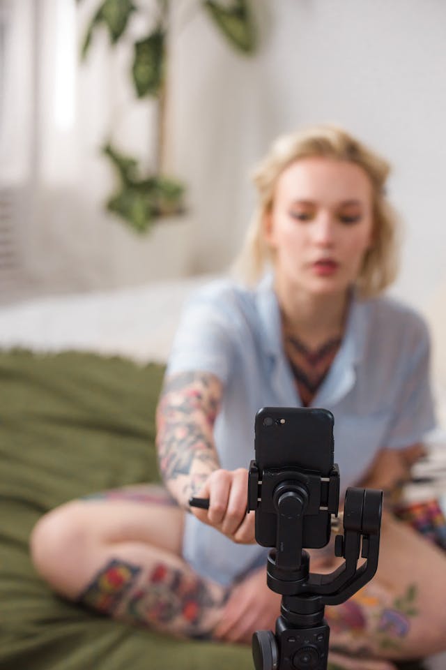 A woman sits down in front of her mounted cell phone and taps the screen.
