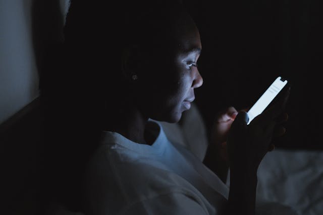 한 여성이 어두운 방에서 휴대폰을 사용하고 있습니다. 