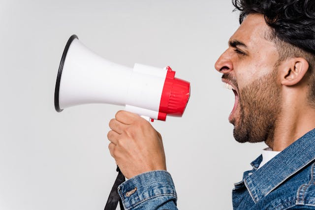 Um homem grita um aviso em um megafone vermelho e branco.