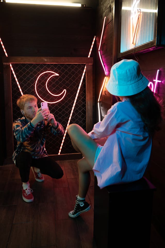 A woman poses in front of her friend with a camera.
