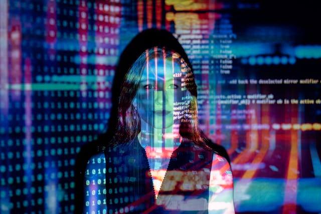 A woman stands in front of a projection of computer code.