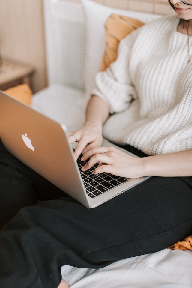 Eine Frau in einem weißen Pullover tippt auf ihrem Laptop.