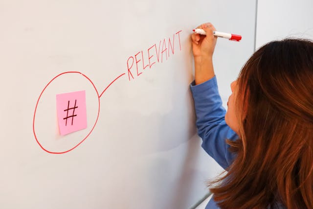 Eine Frau schreibt das Wort "Relevant" auf ein Whiteboard und zeichnet eine Linie, die es mit einem Post-it mit dem Hashtag-Zeichen verbindet.