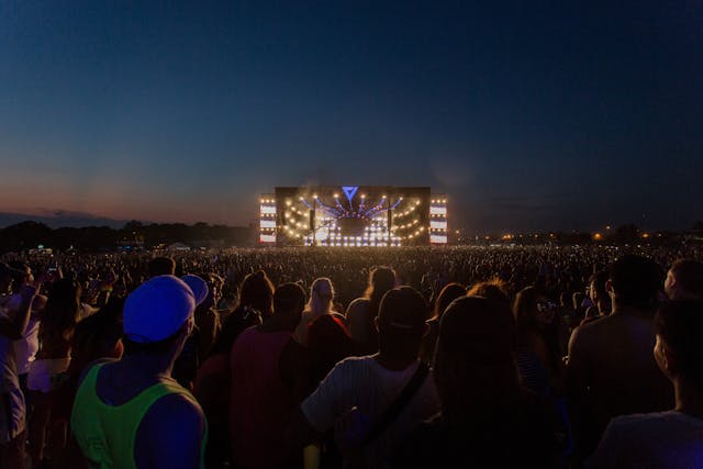 Um grande público se reúne em frente a um palco ao ar livre e aguarda o início do show.