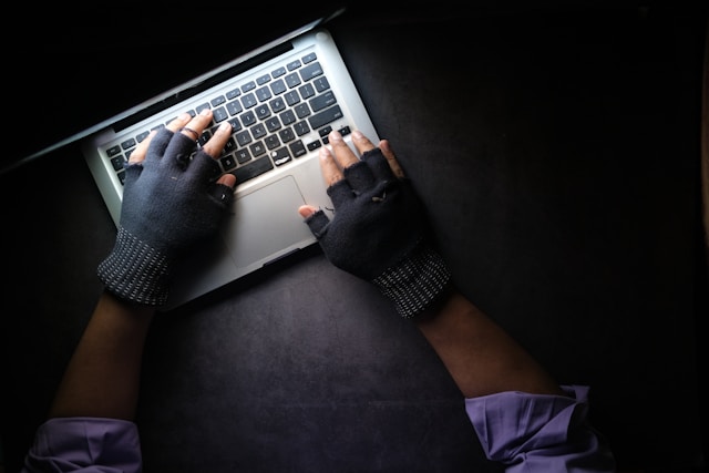 Un anonimo indossa dei guanti e scrive su un computer portatile. 